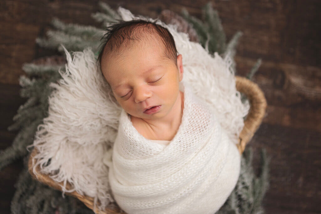 Newborn baby peacefully sleeping, wrapped in a white knit swaddle during a studio newborn photography session in Pawtucket, Rhode Island.
