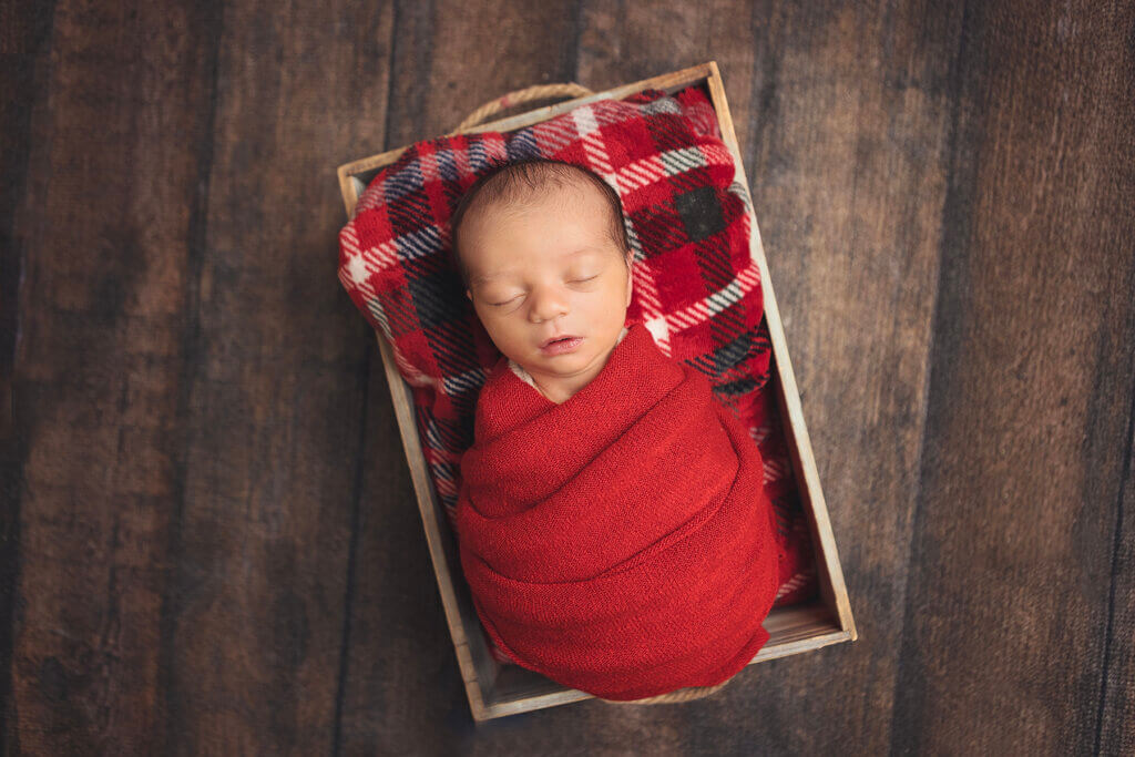 Newborn baby boy posed in a bucket with a festive holiday blanket during a Christmas newborn photography session in Pawtucket, Rhode Island.